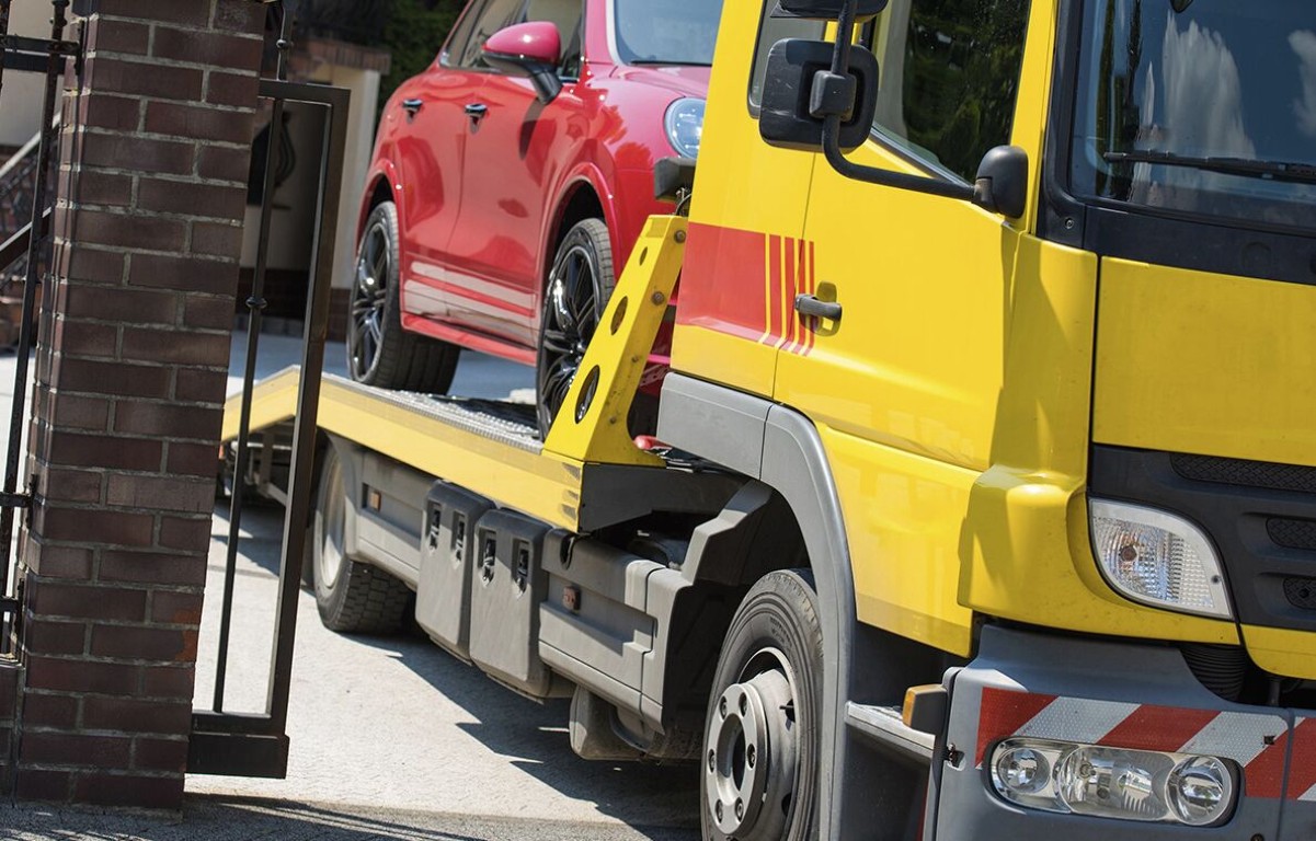 Yellow flatbed tow truck safely transporting a red car in Cardiff, CA